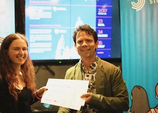 Person handing out award certificate to a student, shaking hands.