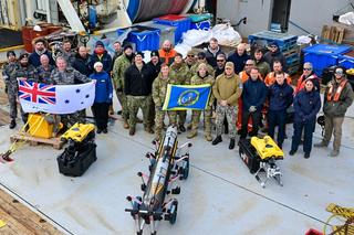 US Navy, Royal Navy and Royal Australian Navy personnel pose for a picture with Mission Specialist Defender Mark IV remotely-operated vehicles and an IVER4 900 autonomous underwater vehicle during the AUKUS Pillar II Subsea and Seabed Warfare Event Two/Integrated Battle Problem 25.1, Atlantic Ocean, June 2024.